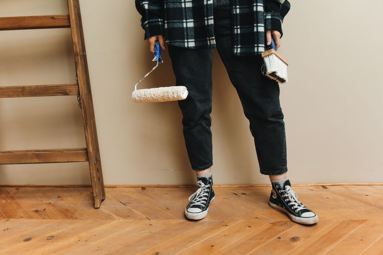 A person holding a paint roller and brush during a home renovation project.